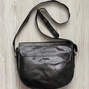 May include: A black leather shoulder bag with a snakeskin pattern. The bag has a gold buckle and a long strap.