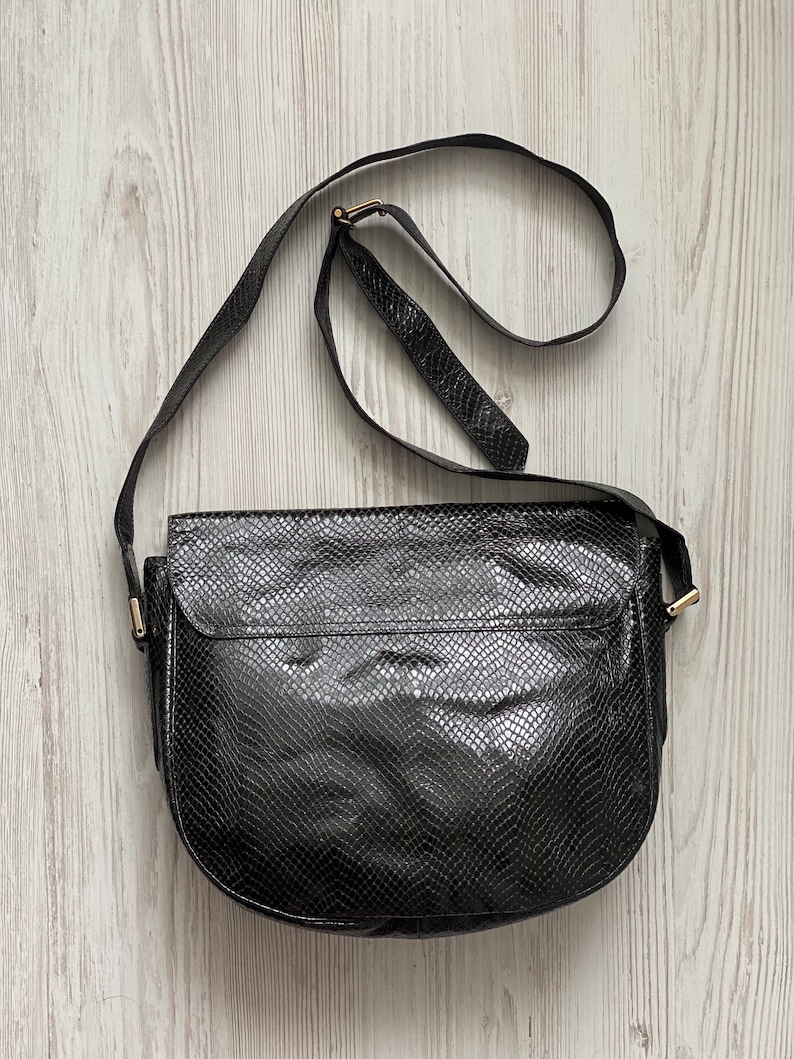 May include: A black leather shoulder bag with a snakeskin pattern. The bag has a gold buckle and a long strap.