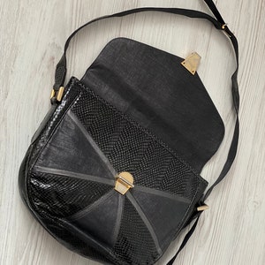 May include: A black leather shoulder bag with a snakeskin pattern and gold hardware. The bag has a flap closure and a long adjustable strap.
