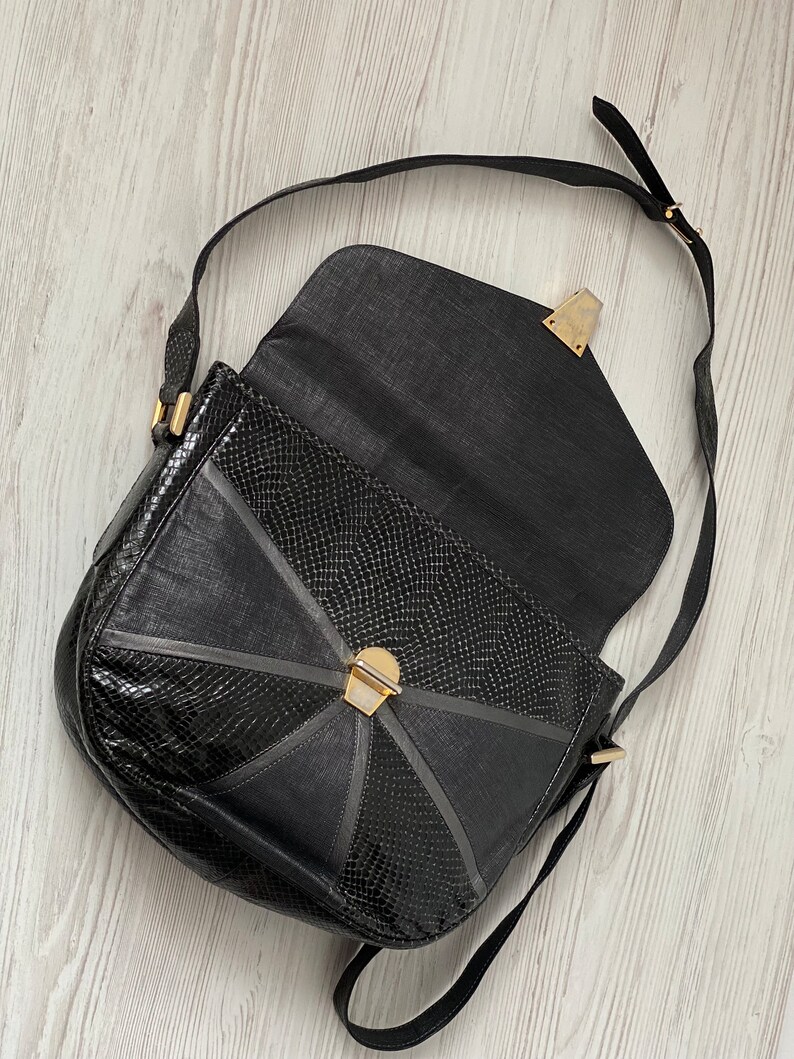 May include: A black leather shoulder bag with a snakeskin pattern and gold hardware. The bag has a flap closure and a long adjustable strap.