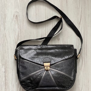 May include: A black leather shoulder bag with a geometric design and a gold clasp.