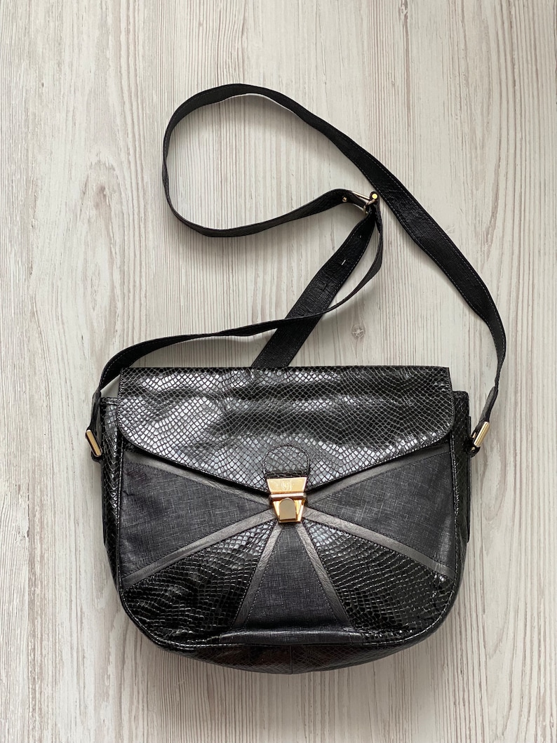 May include: A black leather shoulder bag with a geometric design and a gold clasp.