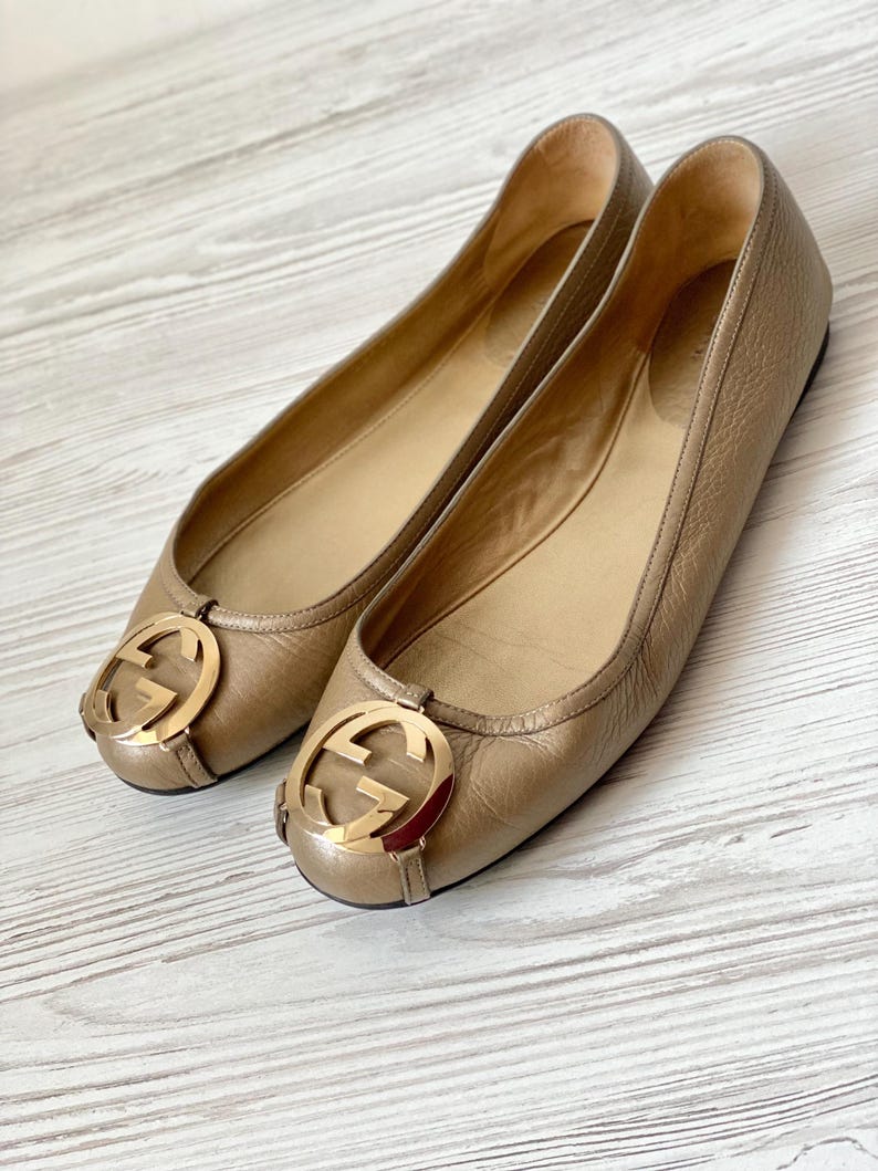 K&ouml;nnte beinhalten: Ein Paar goldene Ballerinas aus Leder mit einem goldenen, ineinandergreifenden G-Logo an der Spitze.