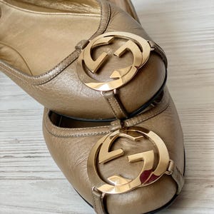 K&ouml;nnte beinhalten: Ein Paar braune Ballerinas aus Leder mit einem goldenen, ineinandergreifenden GG-Logo an der Spitze.