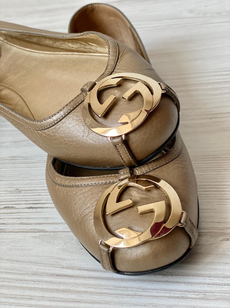 K&ouml;nnte beinhalten: Ein Paar braune Ballerinas aus Leder mit einem goldenen, ineinandergreifenden GG-Logo an der Spitze.