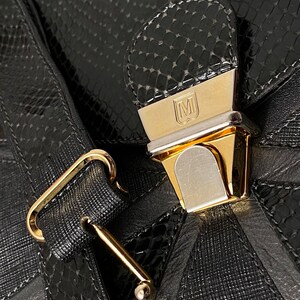 May include: A black leather handbag with a gold-toned clasp and a snakeskin pattern. The clasp has a metal plate with the letter "M" on it.