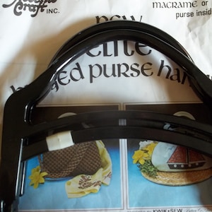 May include: Black plastic purse handle frame. The frame is designed to be used with macrame or fabric to create a purse. The text on the packaging reads "Craft Inc. New Elite Beaded Purse Handles".