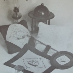 Peut inclure: Image en noir et blanc d'un motif de point de croix représentant un clipper. Le motif est présenté sur trois morceaux de tissu différents, dont un coussin, un petit carré et un grand carré. L'image comprend également un sablier, une lampe et un globe terrestre. Le texte "Clipper Ship" et "Candlewicking & Counted Cross Stitch" est en haut de l'image. Le texte "Krazy Stitches Inc." est en bas de l'image.
