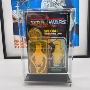 Op de afbeelding: Een Star Wars "The Power of the Force" actiefiguurset, met een gouden munt en een Amanaman-figuur, gepresenteerd in een doorzichtige beschermhoes. De verpakking bevat het Star Wars-logo en de tekst "Special Collectors Coin."