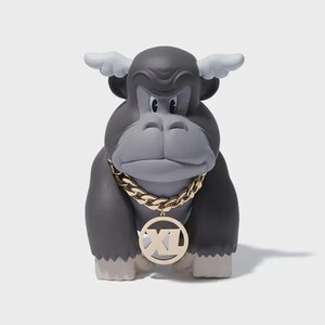 May include: A gray gorilla figurine with white wings and a gold chain necklace. The gorilla has a serious expression and a gold pendant with the letters "XL". The figurine is on a white background.
