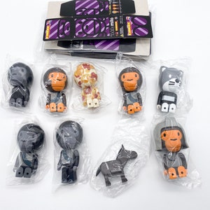 Peut inclure: Une collection de huit petites figurines en plastique colorées dans des sachets en plastique transparent individuels. Les figurines représentent différents personnages, dont des singes, un chat et un cheval. Les figurines sont toutes dans des poses et des expressions variées.