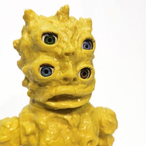 May include: A yellow, textured, humanoid figure with four eyes. The eyes are different colors: green, blue, blue, and brown. The figure has a large, open mouth.