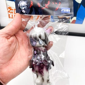 Peut inclure: Une figurine blanche et noire avec des détails violets et blancs. La figurine a un visage de chat avec de grands yeux et un nez noir. La figurine porte une robe à motifs violets et blancs. La figurine est emballée dans un sac en plastique transparent avec une étiquette blanche et noire qui dit "全て商品全てで送料無料".
