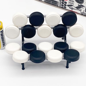 May include: A miniature model of a black and white modular sofa. The sofa is made of 12 individual round cushions, six black and six white, arranged in a staggered pattern. The sofa is sitting on a white surface.