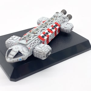Peut inclure: Maquette détaillée d'un vaisseau spatial, principalement grise avec des accents rouges et blancs. Le modèle présente des détails complexes, notamment des composants de moteur et un cockpit. Monté sur une base noire rectangulaire, un objet de collection.