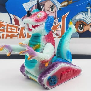 May include: A colorful toy monster with a red, blue, and white head, black horns, and a long tail. The toy has a tank-like base with red and purple accents. The monster is a vibrant mix of colors, including pink, blue, and purple.