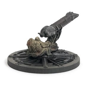 May include: A detailed, gray and black plastic model of a spaceship from the Alien franchise. The spaceship is mounted on a circular base with a detailed design.