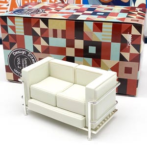 Könnte beinhalten: Weiße Leder-Miniatur-Replik eines klassischen Mid-Century-Modern-Sofas mit verchromten Beinen. Das Sofa ist Teil einer limitierten Design-Innenausstattungskollektion.