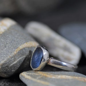 May include: A silver ring with a blue sea glass stone set in a bezel setting.