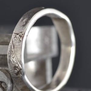 Könnte beinhalten: Ein silberner Ring mit einer strukturierten, leicht gehämmerten Oberfläche. Der Ring ist schlicht und elegant mit einem dezenten Design.