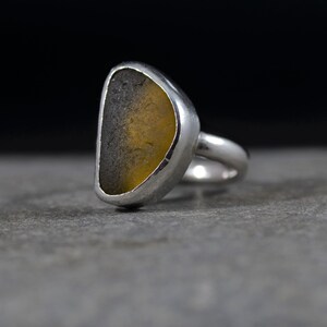May include: A silver ring with a yellow and gray sea glass stone set in the center.