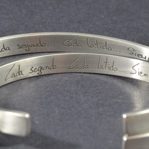 May include: Two silver bracelets with the inscription "Cada segundo... Cada latido... Siempre" engraved on them.