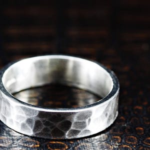 May include: A silver band ring with a hammered texture. The ring is wide and has a rounded profile.
