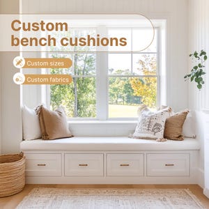 Op de afbeelding: Een witte vensterbank met een wit kussen en twee kussens. De bank heeft drie lades en staat voor een raam met uitzicht op bomen en gras. De tekst "Custom bench cushions" staat boven de bank, met de woorden "Custom sizes" en "Custom fabrics" eronder.