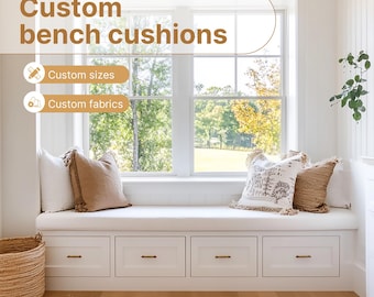 May include: White window seat bench with a white cushion and two throw pillows. The bench has three drawers and is in front of a window with a view of trees and grass. The text "Custom bench cushions" is displayed above the bench, with the words "Custom sizes" and "Custom fabrics" below it.