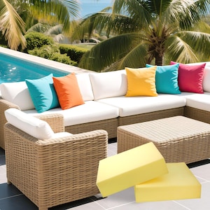 May include: Wicker outdoor sectional sofa with white cushions and vibrant throw pillows in turquoise, orange, yellow, and pink. A matching wicker coffee table and armchair are also present. Two yellow foam cushions are in the foreground. Palm trees and a pool are in the background.