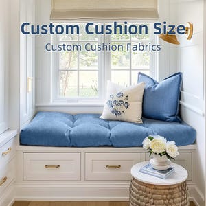 Puede incluir: Un asiento de ventana con un cojín y almohadas azules. Un cojín blanco con bordado floral azul está centrado en el asiento. El texto "Custom Cushion Size" y "Custom Cushion Fabrics" está en la parte superior de la imagen.
