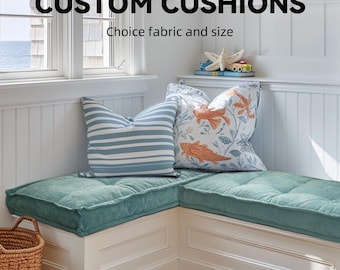 Könnte beinhalten: Eine Eckbank an einem Fenster mit maßgefertigten Kissen. Die Kissen sind blaugrün und haben ein gestepptes Design. Die Bank ist weiß mit weißen Wandverkleidungen. Der Text "CUSTOM CUSHIONS" und "Choice fabric and size" ist über der Bank zu sehen.