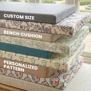 Op de afbeelding: Een stapel rechthoekige bankkussens met diverse patronen en kleuren, waaronder effen grijs, blauwe bloemen, beige klaprozen, effen groenblauw, groene kerstbomen, effen beige en een crèmekleurige stof met rode en groene bloemmotieven in ovalen.