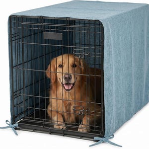 Puede incluir: Una jaula de alambre metálico negro para perros cubierta con una funda de tela azul claro texturizada. La jaula cuenta con una puerta frontal con mecanismo de cierre y un perro de color dorado sentado en el interior. La funda se sujeta con lazos.