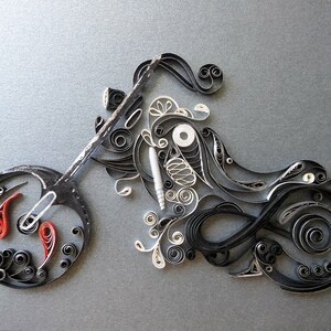 May include: A black and white paper quilling artwork depicting a motorcycle. The motorcycle is made of intricate paper curls and swirls. The motorcycle has a red and white front wheel.
