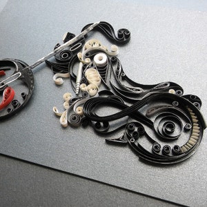 May include: A black and white paper quilling artwork depicting a motorcycle. The motorcycle is made of curled paper strips and has a red and white wheel.