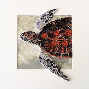 Peut inclure: Une œuvre d'art en papier quilling représentant une tortue de mer avec une carapace noire et orange. La tortue nage dans un fond d'eau bleu clair.
