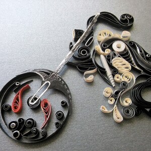 May include: A black and white paper quilling artwork depicting a motorcycle. The motorcycle is made of curled paper strips and has a red and black wheel.
