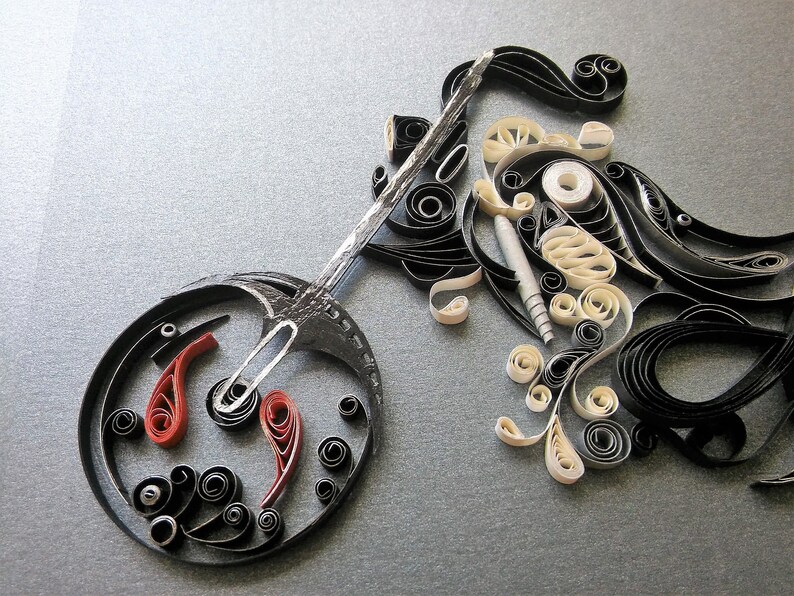 May include: A black and white paper quilling artwork depicting a motorcycle. The motorcycle is made of curled paper strips and has a red and black wheel.