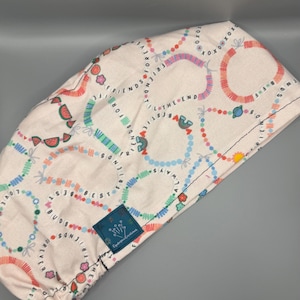 May include: White scrub cap with a colorful pattern of beaded bracelets, watermelon slices, and the phrases "Best Friends Forever" and "Love Always." The cap has a drawstring and a small blue label.