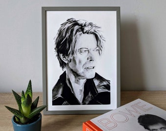 May include: A black and white framed print of a portrait of David Bowie. The print is on a white background and the image is of Bowie's face and shoulders. He is wearing a black jacket and has short, dark hair.