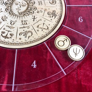 K&ouml;nnte beinhalten: Ein Holzspielbrett mit einem kreisf&ouml;rmigen Zodiak-Design und einer transparenten Acrylabdeckung. Die Abdeckung hat die Zahlen 4 und 6 aufgedruckt. Zwei Holzmarker mit Symbolen befinden sich auf dem Brett.