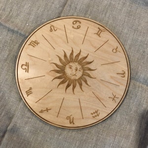 K&ouml;nnte beinhalten: Ein rundes Holzrad mit den Tierkreiszeichen und einer Sonne mit einem Gesicht in der Mitte.