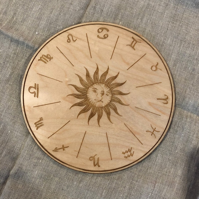 K&ouml;nnte beinhalten: Ein rundes Holzrad mit den Tierkreiszeichen und einer Sonne mit einem Gesicht in der Mitte.