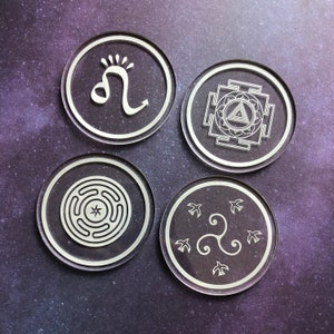 May include: Four white coasters with different designs. The first coaster features a stylised lion symbol, the second has a geometric design with a triangle in the centre, the third has a circular design with a star in the centre, and the fourth has a stylised triskelion symbol.