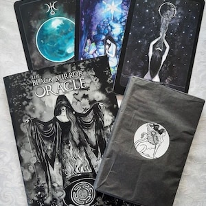 May include: The Black Mirror Oracle deck with a black and white illustration of a woman in a long black robe holding strings connected to a cauldron. The deck is on a gray surface with a black and white illustration of a winged creature on a gray bag.