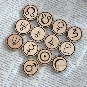 K&ouml;nnte beinhalten: Ein Satz von 12 astrologischen Holzschaftmarken. Jede Marke ist ein Kreis mit einem anderen astrologischen Symbol, das in sie geschnitzt ist. Die Marken sind in einem Kreis auf einem St&uuml;ck Papier mit Text angeordnet.