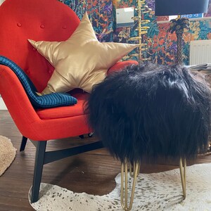 May include: A red armchair with a gold star-shaped pillow and a black fluffy ottoman with gold legs. The chair and ottoman are on a white cowhide rug.