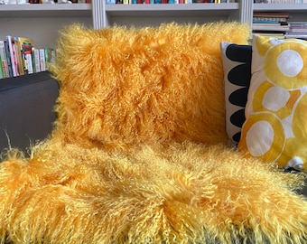 May include: A yellow fluffy sheepskin throw pillow and a matching throw blanket on a black leather couch.