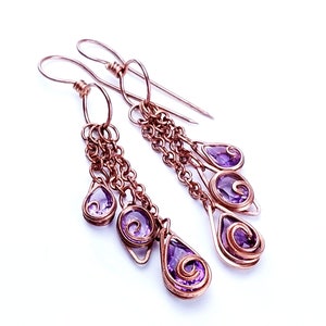 May include: A pair of dangle earrings with multiple amethyst stones set in copper wire. The earrings feature a chain-like design and are finished with a simple hook closure.